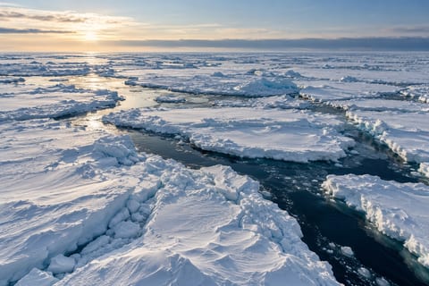Hvide isflager med sne ligger mellem mørkeblå render under lavt polarlys.